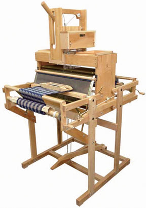 A Leclerc Diana 24" 16-Shaft, Computer Dobby Floor Loom from Leclerc Looms features intricate components such as pedals, heddles, and a shuttle. A partially woven piece of fabric with a pattern in progress can be seen on the sturdy loom, highlighting its traditional weaving craftsmanship.