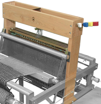 Image of a wooden loom used for weaving. The Leclerc Looms Dorothy 4-shaft section features a sturdy wooden frame with metal components and yarn threads stretched across it. On the right side, there's a lever with red, yellow, and blue handles. Some fabric is partially woven on the loom.