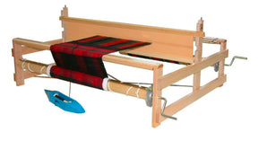 The Leclerc Bergere Rigid Heddle Loom, 24" by Leclerc Looms showcases a partially woven black and red fabric. The wooden frame supports various rods and levers, with ratchet brakes ensuring precision. A blue shuttle rests on the loom, while metal components adjust tension and fabric positioning.