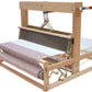 Image of the Leclerc Dorothy Table Loom by Leclerc Looms, showcasing threads in various colors. This collapsible loom features a large frame with several heddles and a roller where completed fabric is being wound. The 4-shaft loom is set up for weaving, with yarn stretched across the warp and fabric forming the weft.