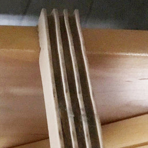 Close-up image of the edge of a multi-layered piece of light-colored plywood revealing its thin layers bonded together, showcasing a slightly rough texture typical of a standard wood finish. Leclerc Rubber Bumper Under Shaft Pads for Floor Looms (ea) by Leclerc Looms can be used with this plywood to reduce noise and absorb impact.