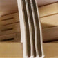 A close-up image of a wooden slat made from several thin layers of wood glued together. The multi-layered, laminated structure is placed on a wooden surface. In the background, Leclerc Rubber Bumper Under Shaft Pads for Floor Looms by Leclerc Looms are visible, helping to absorb impact and reduce noise.