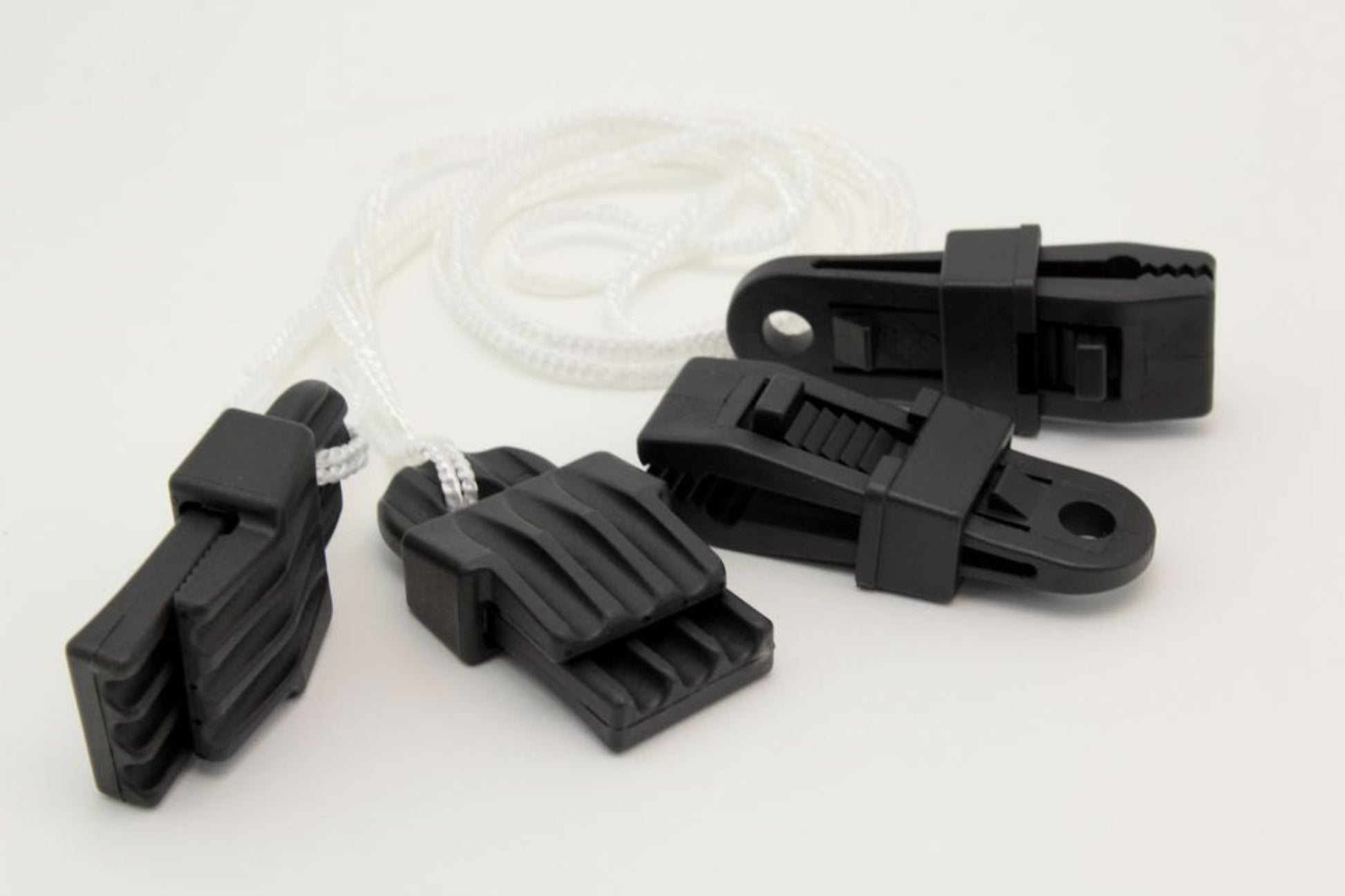 Four Leclerc Clip Temple accessories, made of black plastic with jagged teeth, are attached to a white cord and arranged on a plain white background. These innovative clips from Leclerc Looms feature a textured grip and an eyelet hole for secure attachment, making them ideal for use with Leclerc looms and other weaving projects.