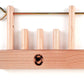 The Leclerc Looms Leclerc Shaft Stabilizer is a wooden puzzle featuring four vertical pegs of varying heights mounted on a rectangular base, reminiscent of the threading shafts on countermarch looms. It includes a metal rod with a ring handle that slides through holes at the top of the pegs to secure them in place. The base also displays a stamped logo of a person's head.