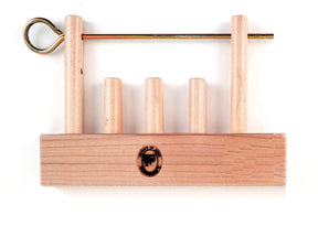 The Leclerc Looms Leclerc Shaft Stabilizer is a wooden puzzle featuring four vertical pegs of varying heights mounted on a rectangular base, reminiscent of the threading shafts on countermarch looms. It includes a metal rod with a ring handle that slides through holes at the top of the pegs to secure them in place. The base also displays a stamped logo of a person's head.