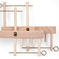 The Leclerc Threading Helper by Leclerc Looms features several pieces, including rectangular wooden blocks and brass rods with looped ends, all arranged in a visually complex configuration. The elements are interlocked like a harness stabilizer, creating an intriguing 3D structure.