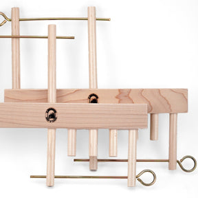 The Leclerc Threading Helper by Leclerc Looms features several pieces, including rectangular wooden blocks and brass rods with looped ends, all arranged in a visually complex configuration. The elements are interlocked like a harness stabilizer, creating an intriguing 3D structure.