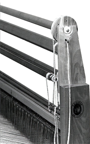 A black and white close-up photo of a Leclerc Shed Regulator wooden weaving loom by Leclerc Looms. The loom features rods for holding threads and a mechanism with pulleys and strings for operating it. The frame bears a distinct logo with text engraved on its side.