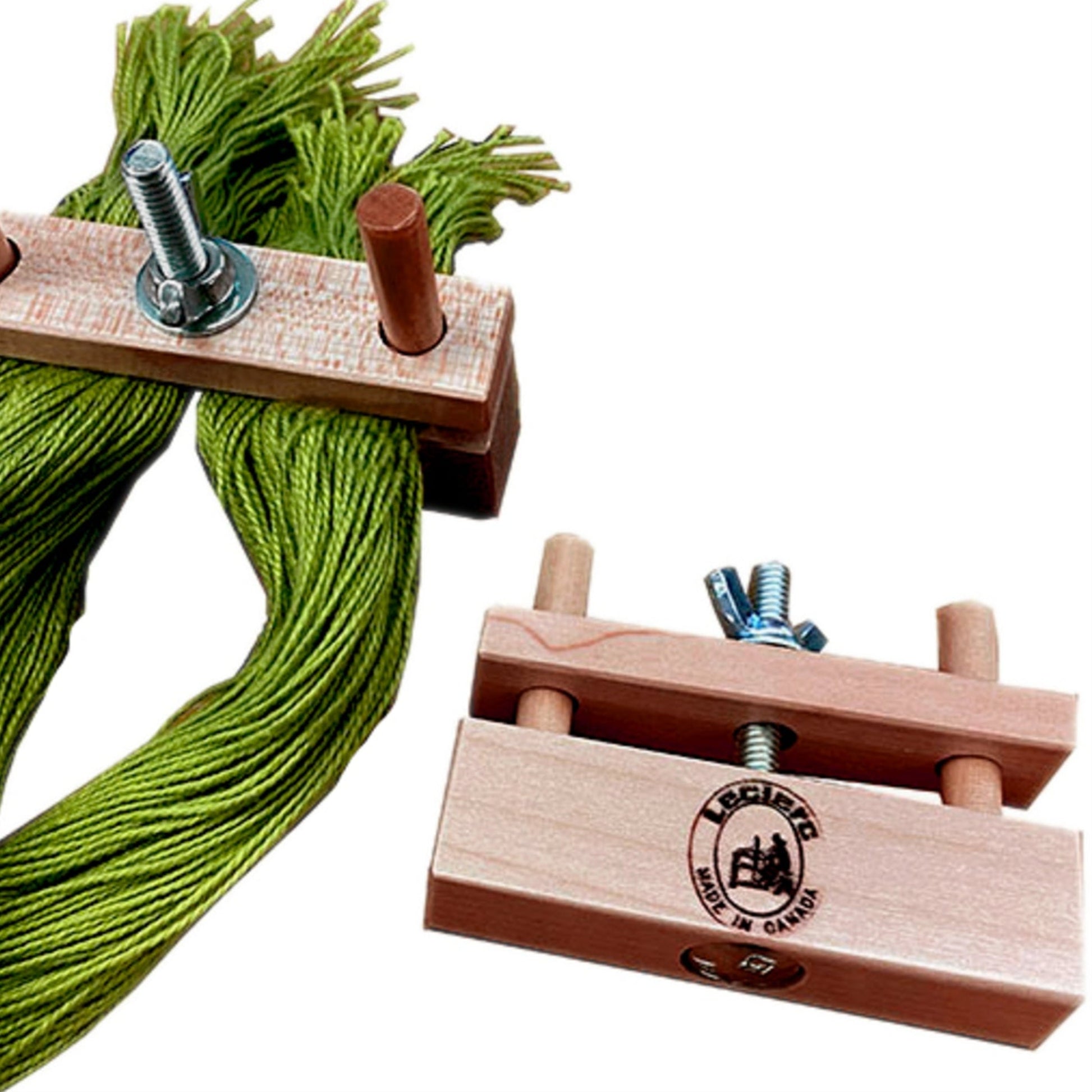 Close-up of two Leclerc Warp-Cross Locks on a white background. One tool is clamped onto green yarn, while the other sits nearby with no yarn attached. Both have metal bolts for adjustments and the Leclerc Looms logo visible.