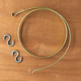 A Leclerc Replacement Flat Steel Brake Circle for Loom, featuring a coiled metal wire with looped ends, is placed on a wooden surface alongside two S-shaped metal hooks by Leclerc Looms. This arrangement implies that the wire and hooks could be intended for hanging or securing items.