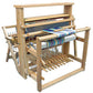 A Leclerc Nilus II 8-Shaft Floor Loom from Leclerc Looms, featuring intricate patterns created by colorful threads woven into fabric in progress. The loom is equipped with multiple levers, frames, and threads to achieve detailed designs.