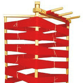 Image of the Leclerc Warping Reel - vertical by Leclerc Looms, featuring a wooden frame structure with horizontal beams. Red ribbons are wound and intertwined around the beams, creating a zigzag pattern. The top of the frame has four exposed beams where the ribbon starts or ends.