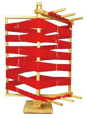 A Leclerc Warping Reel - vertical by Leclerc Looms, featuring bright red yarn wound around it. The reel has multiple pegs extending horizontally to secure the yarn as it rotates smoothly. The yarn is wrapped tightly and organized, and the warping reel is mounted on a sturdy wooden base.