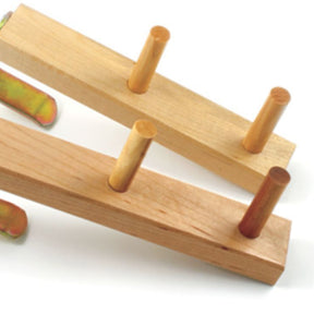 Two Leclerc Warping Pegs from Leclerc Looms, each featuring three cylindrical dowels, are placed on a white surface. The light-colored wooden pegs are positioned parallel to each other, with metal brackets partially visible beside them.