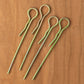 Four Leclerc Treadle Hooks from Leclerc Looms, in green metal, are arranged parallel to each other on a wooden surface. The hooks have a bent shape with looped ends.