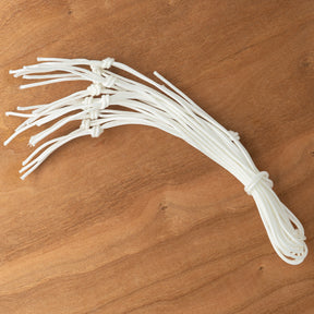 A pack of Leclerc Treadle Cords from Leclerc Looms, featuring white cords with multiple knots, is laid out on a wooden surface.