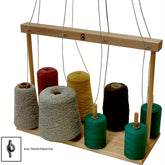 The Leclerc Looms' Leclerc 8-Peg Cone & Tube Holder is a wooden tabletop yarn organizer with multiple spools of yarn in various colors, including red, yellow, green, and brown. It features vertical rods and horizontal thread guides to efficiently guide the yarn. Additionally, it includes a warping paddle for ease of use. An inset image depicts an Easy Thread Pigtail Eye.