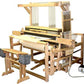 The Leclerc Weavebird V2 Floor Loom by Leclerc Looms features a wooden frame equipped with spools, strings, and a weft mechanism as well as a reed for weaving. It includes two padded foot pedals attached to the structure, and some fabric is already woven and rolled onto the loom.