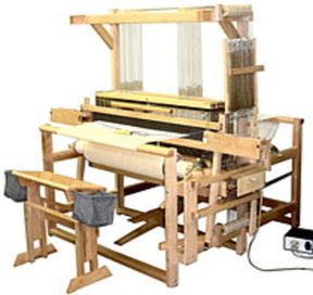 The Leclerc Weavebird V2 Floor Loom by Leclerc Looms is set up for weaving, featuring a wooden frame with pedals, beams, and threads. The machine has a rectangular structure with various mechanical parts, including foot pedals used for operation. An electric control box on the floor is connected to the loom.