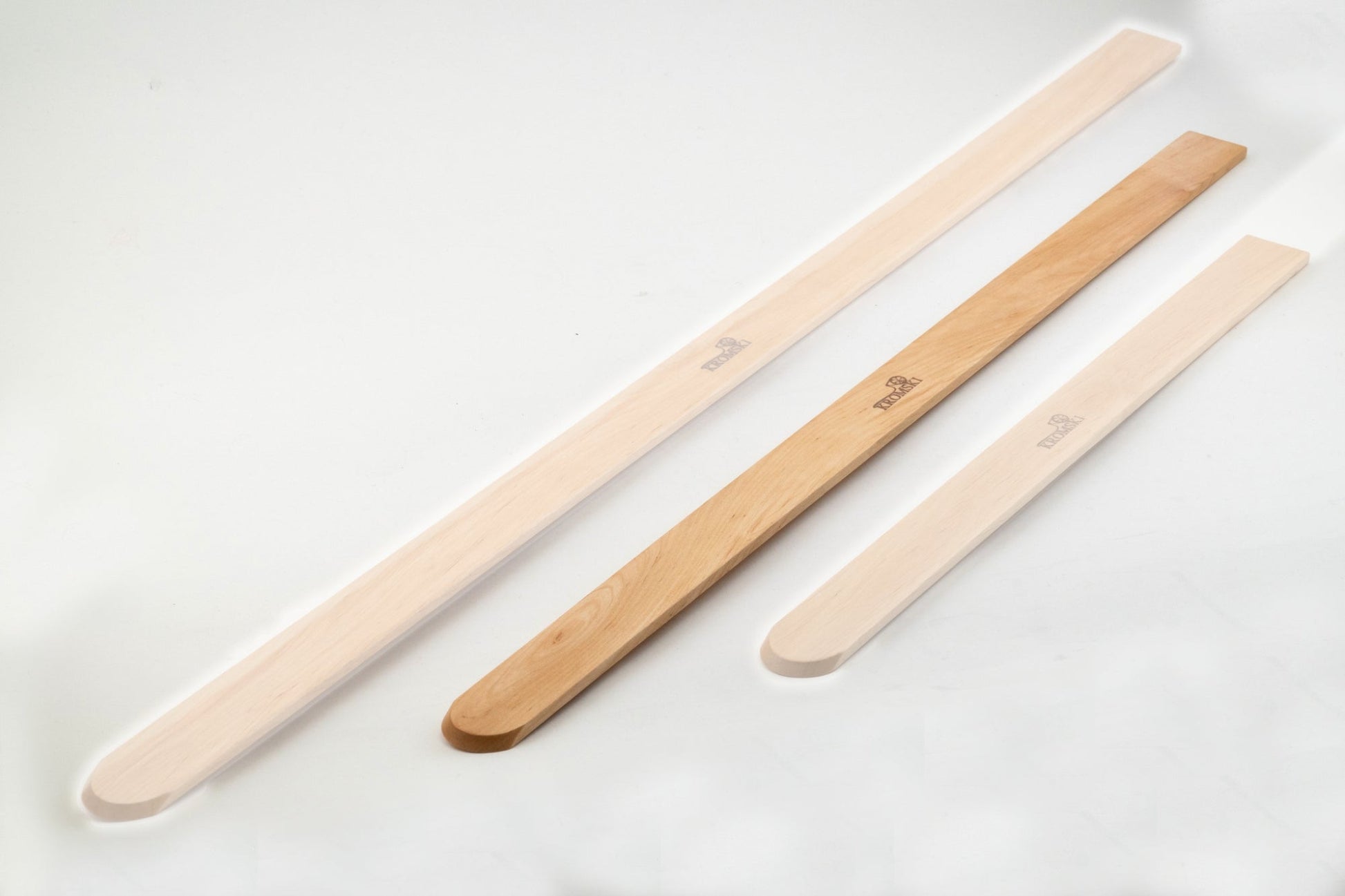 Three Kromski Pickup Stick Clear tools from Kromski North America are arranged parallel to each other on a white background. They vary in size, with the largest on the left, a medium-sized stick in the middle, and the smallest on the right. These weaving tools have a flat, elongated shape and a rounded end.