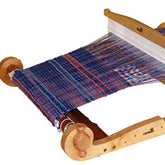 A wooden Kromski Harp Forte Rigid Heddle Loom from Kromski North America with a partially completed piece of blue and orange fabric. The threads are woven tightly, and the loom's structure is simple, emphasizing functionality. The fabric extends from one side to the other, showing progress in the weaving process.