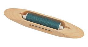 The Schacht Boat Shuttle by Schacht Spindle Co. features a smooth, elongated oval shape with a hollowed-out middle section that holds a spool of teal thread in the center.