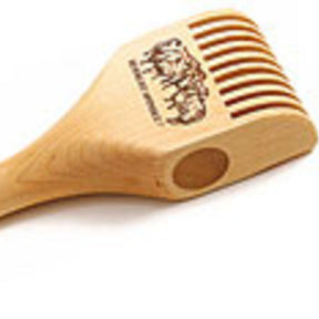 The Schacht Weighted Tapestry Beater by Schacht Spindle Co. is a hefty, light-colored wooden tool featuring a handle with an inset, ergonomic grip and a comb-like end for scratching. It boasts a carved design of an elephant near the top with text above it.