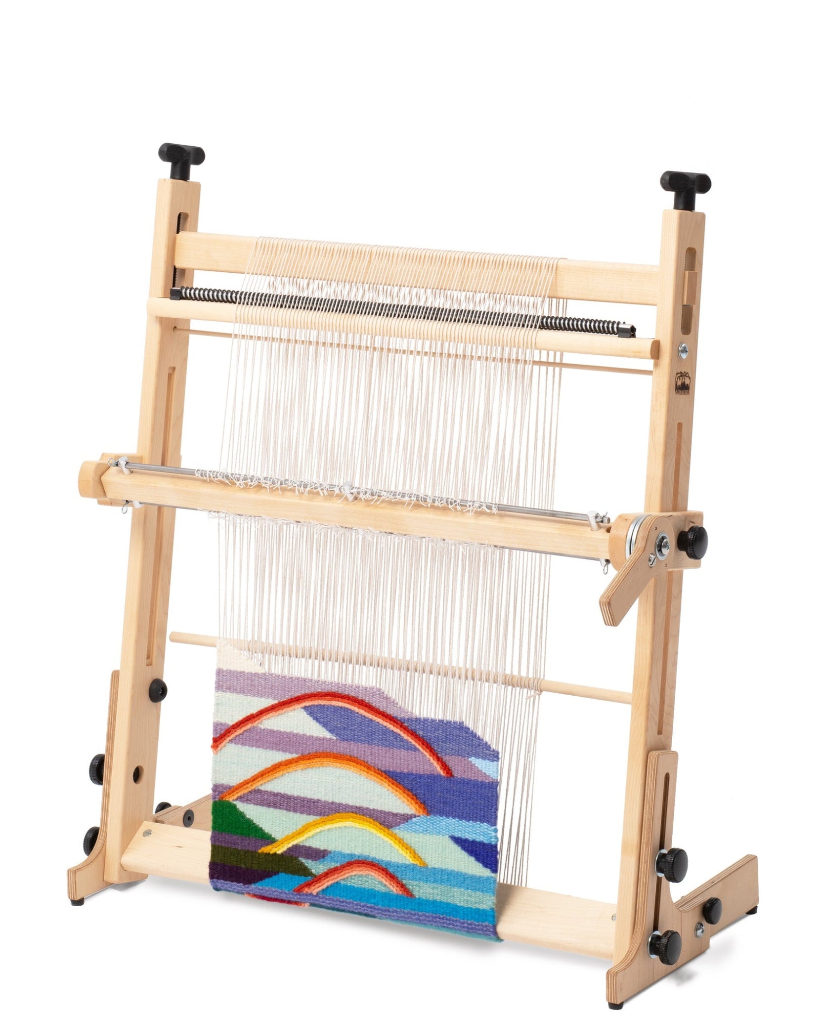 The Arras 20" Tapestry Loom by Schacht is displayed on a white background, highlighting a colorful weaving in progress. The product, crafted from maple hardwood and equipped with precise tension control, showcases an unfinished woven design featuring abstract, intersecting shapes in vibrant colors including red, blue, yellow, and purple.