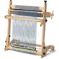 An Arras 20" Tapestry Loom Beam Kit from Schacht Spindle Co., set up with threads ready for weaving. The loom features various knobs and mechanisms for adjusting tension, employing a traditional warping technique. A section of colorful woven fabric is visible at the bottom. The plain white background highlights the loom's structure.