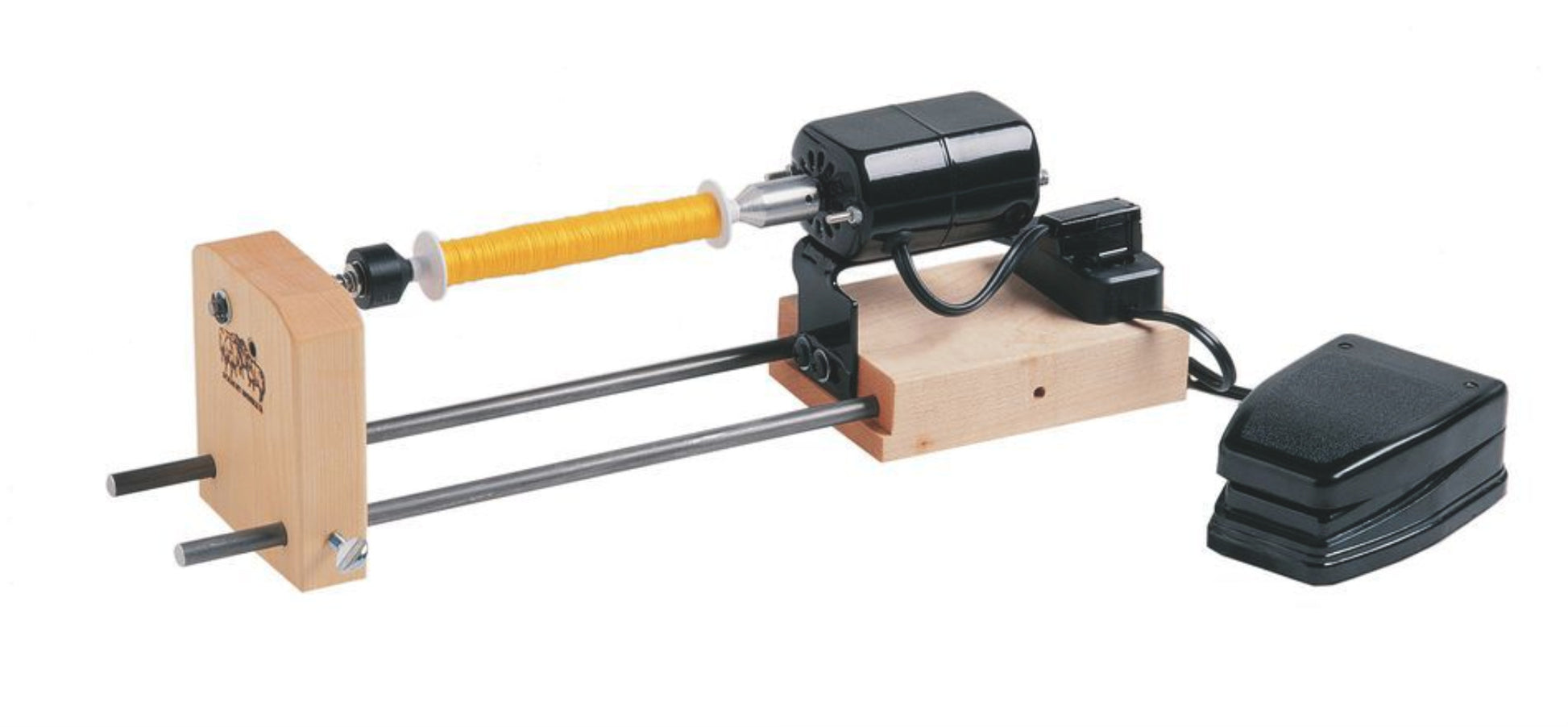 The Schacht Double-Ended Electric Winder by Schacht Spindle Co. is shown. This device, featuring an electric motor and foot pedal, securely holds a yellow thread spool in position on a wooden base supported by two metal rods, providing hands-free operation for crafting fishing flies.