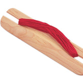 The Ashford Belt Shuttle for Inkle Loom - 18cm / 7" by Ashford Handicrafts Limited, with two long prongs, holds a loop of red yarn displayed on a white background. The yarn is neatly wound around the prongs, indicating it is ready for use in weaving or crafting projects on a belt loom.
