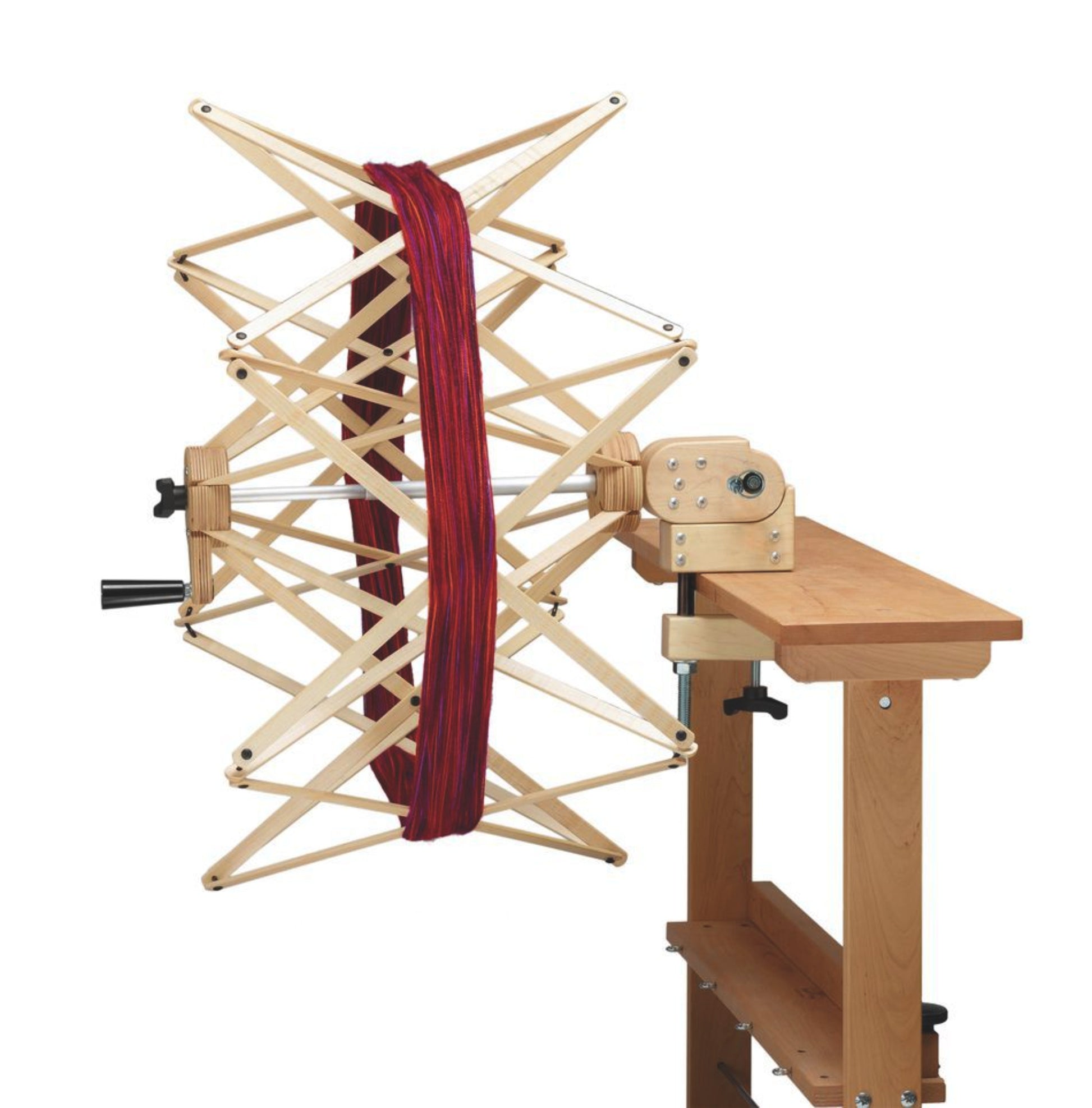 A Schacht Ultra Umbrella Swift yarn winder from Schacht Spindle Co., holding a skein of red yarn, is attached to a wooden table. The swift is fully extended, accommodating skeins up to 93 inches, and the table features a clamp for secure attachment. The overall setup, complete with an optional counter, is ready for winding yarn into balls.