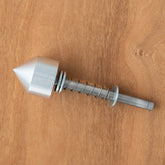 A sleek silver metal component with a pointed conical tip from the Schacht Double Ended Electric Bobbin Winder Live Center Replacement Kit by Schacht Spindle Co. rests on a wooden surface. Its design, featuring a coil spring and rod, highlights precision engineering for efficient use.