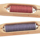 Two Schacht Boat Shuttles from Schacht Spindle Co. used for weaving, each containing a bobbin of thread. The top shuttle holds red thread, while the bottom shuttle holds dark purple thread. The smooth, elongated designs of the shuttles are visible, emphasizing their craftsmanship.