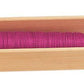 A Schacht End Delivery Shuttle from Schacht Spindle Co. is loaded with a bobbin of pink thread. The shuttle, similar to those used for Schacht Pirns, features an elongated design with a carved-out section to hold the bobbin and a metal piece at one end to guide the thread, ensuring even tension.