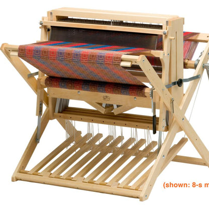 A Schacht 26" Baby Wolf Floor Loom by Schacht Spindle Co. with a colorful woven cloth partially completed. The loom, which is shown on a stand, includes multiple shafts for weaving complex patterns.