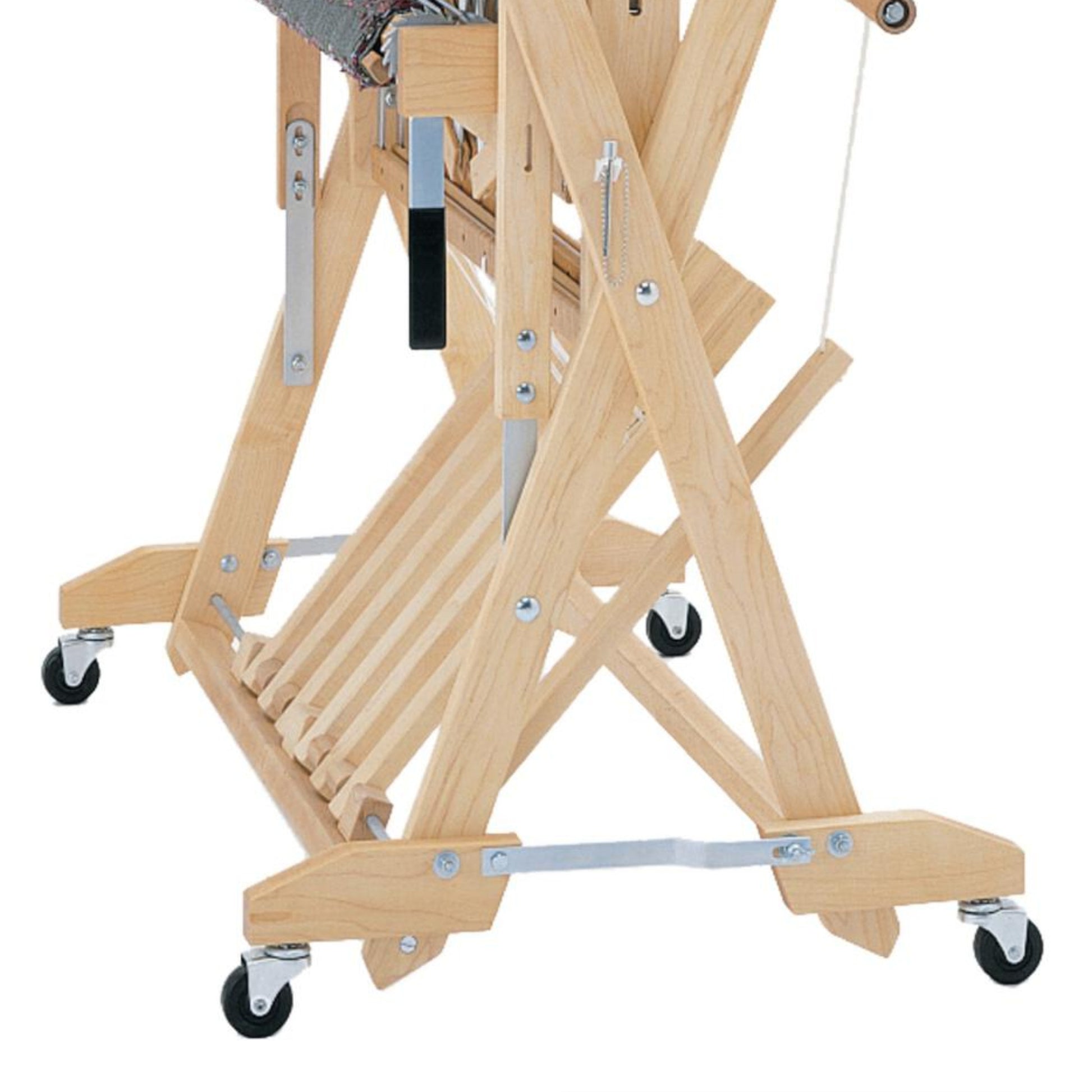 A close-up view of the base and legs of a wooden Schacht Wolf Stroller from Schacht Spindle Co. on caster wheels. The light-colored wood frame features various metal fittings and supports designed for adjusting and securing the loom's position. The wheels aid in mobility.