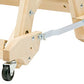 Close-up view of the lower part of a wooden Schacht Wolf Stroller by Schacht Spindle Co., featuring metal brackets, screws, and small caster wheels. The structure appears to be part of a larger, possibly movable loom or piece of furniture.