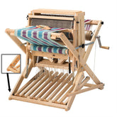 A Schacht 18" Wolf Pup Floor Loom by Schacht Spindle Co., featuring unfinished woven fabric in teal, purple, and white. The loom is equipped with multiple treadles, warp threads, and a side crank. An inset image highlights a close-up of a wooden component.