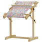 An adjustable wooden weaving loom with a colorful striped fabric partially woven sits on the sturdy Schacht Trestle Floor Stand for Flip Looms by Schacht Spindle Co. The stand comes equipped with multiple knobs for adjusting the frame position and features adjustable width supports to accommodate various sizes. The vibrant striped fabric adds a lively touch to the setup.