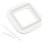 A Schacht Zoom Loom 4" x 4" from Schacht Spindle Co. is a white square object with rounded corners and parallel diagonal grooves along its edges. Beside it, there are two thin needles positioned parallel to each other on a white background, resembling tools from the weaving kit.