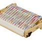 The Schacht Flip Folding Rigid Heddle Loom by Schacht Spindle Co. is a wooden weaving loom designed with colorful threads arranged in a pattern. It features knobs and levers for adjusting tension and position, showcasing vibrant threads in shades of red, blue, yellow, green, and purple. This folding rigid heddle loom is perfect for two-heddle weaving intricate fabrics.