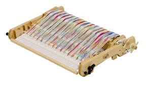 The Schacht Flip Folding Rigid Heddle Loom by Schacht Spindle Co. is a wooden weaving loom designed with colorful threads arranged in a pattern. It features knobs and levers for adjusting tension and position, showcasing vibrant threads in shades of red, blue, yellow, green, and purple. This folding rigid heddle loom is perfect for two-heddle weaving intricate fabrics.