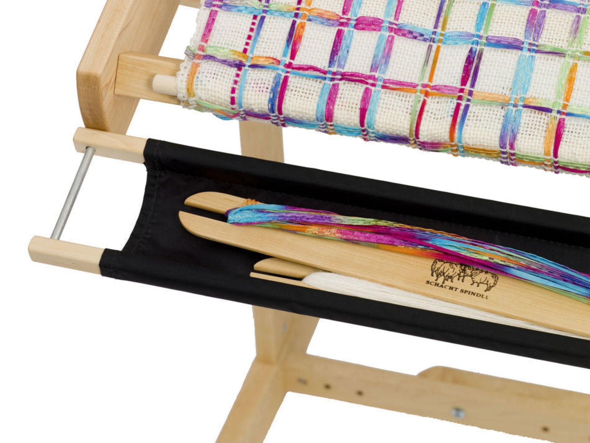 A Schacht Flip Trap weaving loom from Schacht Spindle Co., featuring a bright multicolored fabric partially woven on it. Beneath the woven fabric, there is a black cloth pouch holding several shuttles, including one wooden shuttle with colorful yarn wrapped around it, all elegantly supported by a Schacht trestle stand.