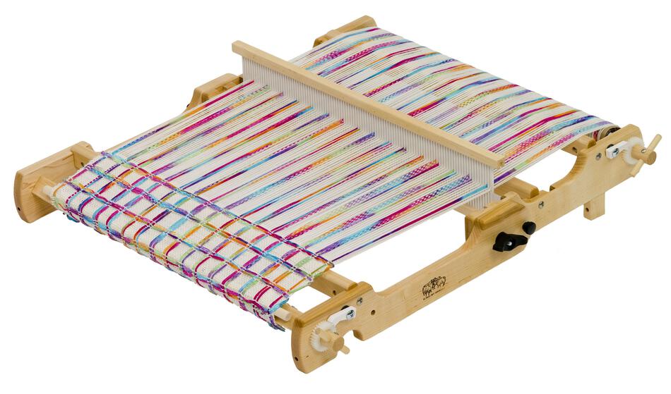 The Schacht Flip Folding Rigid Heddle Loom by Schacht Spindle Co. boasts multicolored threads stretched across its frame, which is equipped with pegs and adjustable mechanisms for precise tensioning of the threads. At its center is a comb-like reed to assist in the weaving process, making it an ideal tool for both beginners and those following warping and weaving instructions.