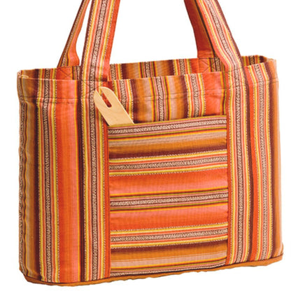 A vibrant and colorful Cricket Loom Bag from Schacht Spindle Co. features an alternating stripe pattern of various widths and textures, with shades of orange, red, and yellow. The bag has two fabric handles and includes an external pocket that holds a wooden comb.