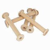 A set of four Harrisville 4" Wood Bobbins from Harrisville Designs, which resemble the tools used by weavers, is scattered on a white surface. These light brown, cylindrical bobbins with circular ends have a simple, rustic appearance and are empty, without any thread or yarn wound around them.