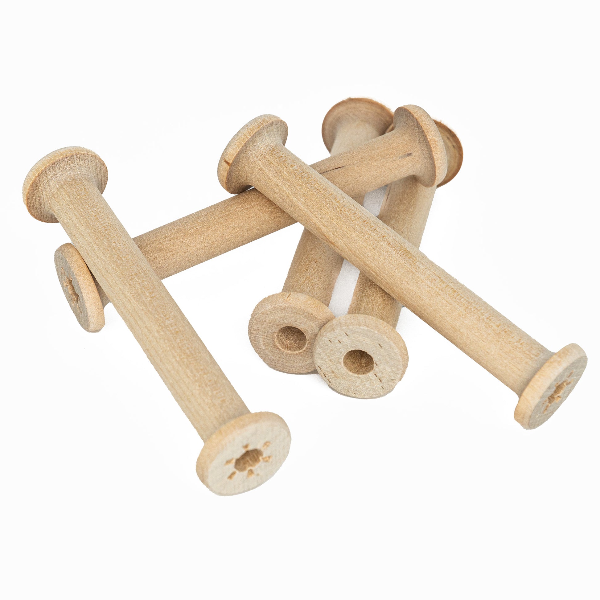 A set of four Harrisville 4" Wood Bobbins from Harrisville Designs, which resemble the tools used by weavers, is scattered on a white surface. These light brown, cylindrical bobbins with circular ends have a simple, rustic appearance and are empty, without any thread or yarn wound around them.