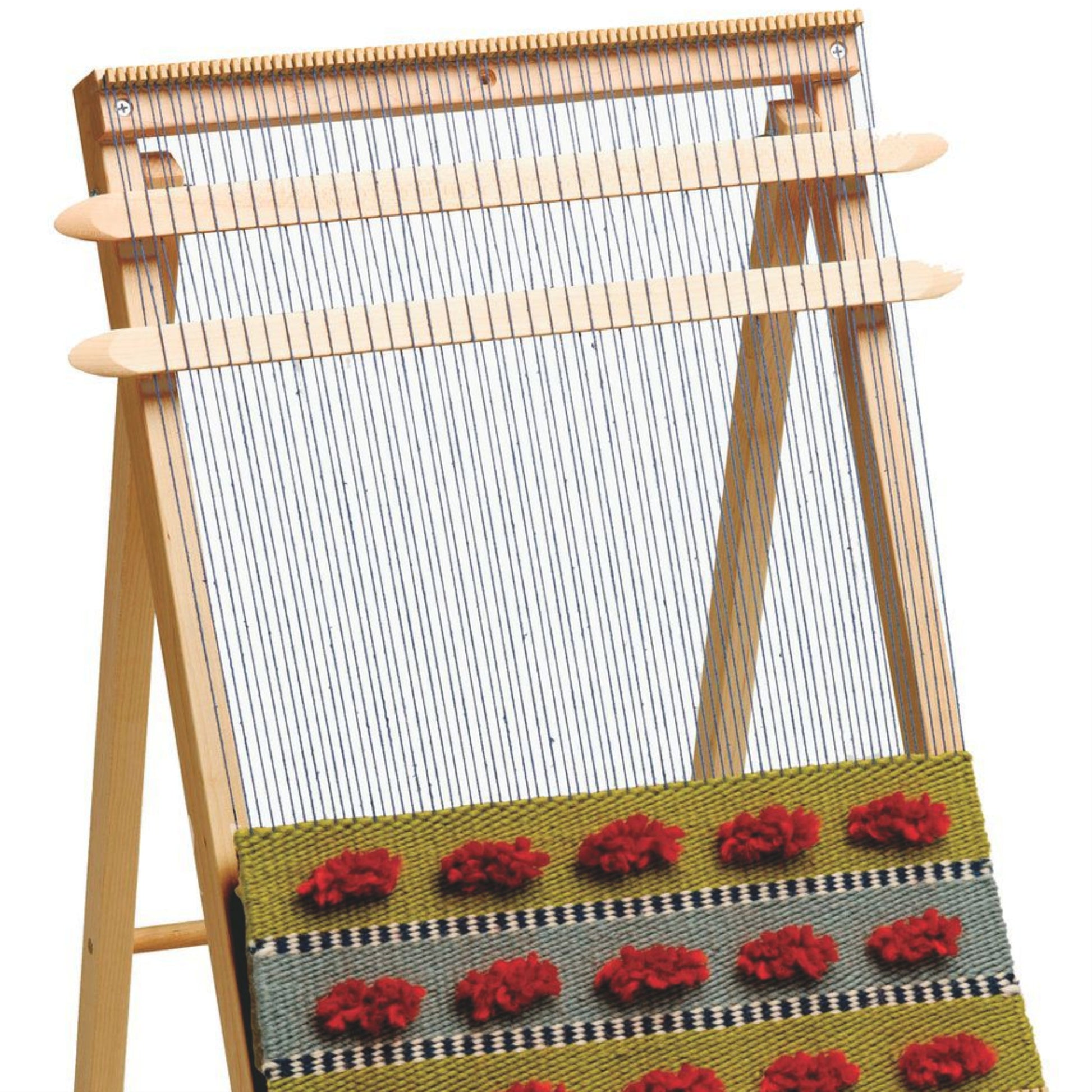 The Schacht School Loom from Schacht Spindle Co. stands upright with thin strings vertically stretched across it. The started woven fabric at the base features a yellow-green background with rows of red textured flowers separated by black-and-white checkered sections. A weaving needle rests nearby, ready for the next row.