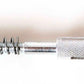 The Schacht Heddle Bar Hook by Schacht Spindle Co. is a metal tool featuring a slender, extended coiled spring at one end and a knurled, textured cylindrical grip in the middle for better handling. The opposite end is designed with a hexagonal fitting, making it ideal for use as a heddle bar hook on Schacht Wolf looms.